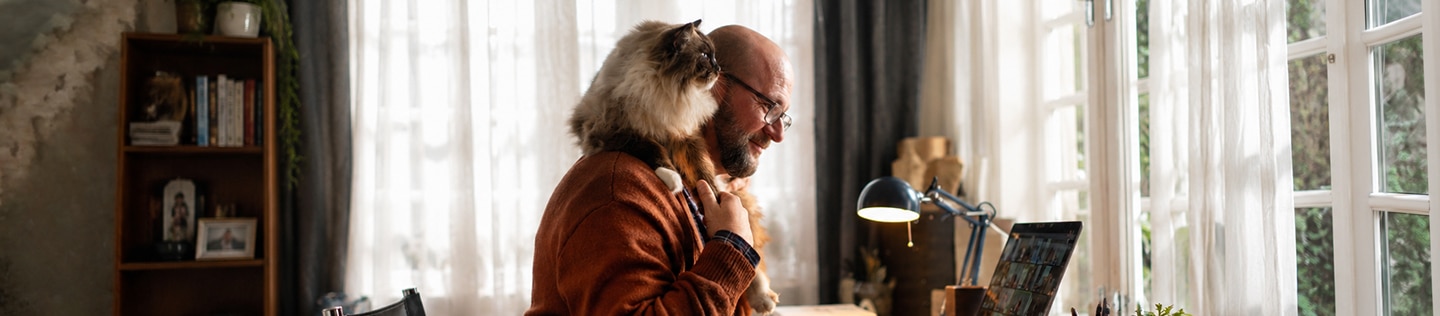 Homme assis devant un ordinateur, souriant, avec un chat aux poils soyeux perché sur son épaule