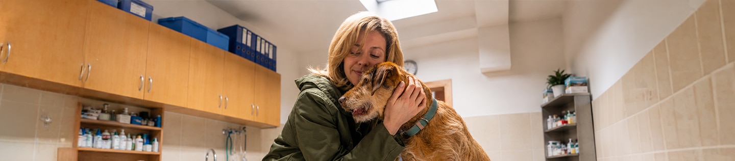 Une femme souriante, les yeux fermés, en train de câliner un chien de taille moyenne au pelage fauve
